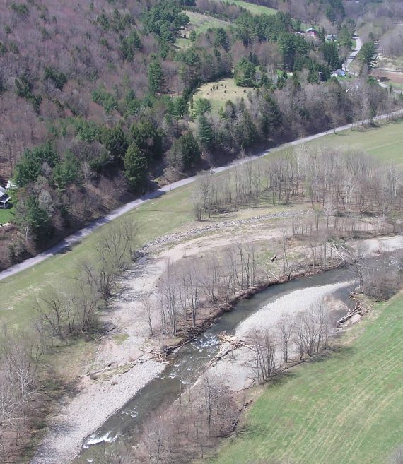 Drone view of river valley with mountains rising up on left side.